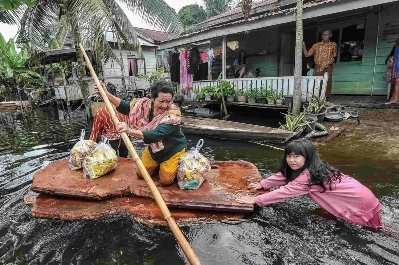 Warga menggunakan kayu untuk melintasi kawasan permukiman yang terendam banjir di Penyengat Rendah, Jambi, Senin (17/03).
